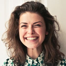 Close-up portrait of a smiling woman with curly hair wearing a patterned blouse.
