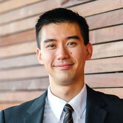 Close-up portrait of a professional man wearing a suit and tie, standing against a wooden background.